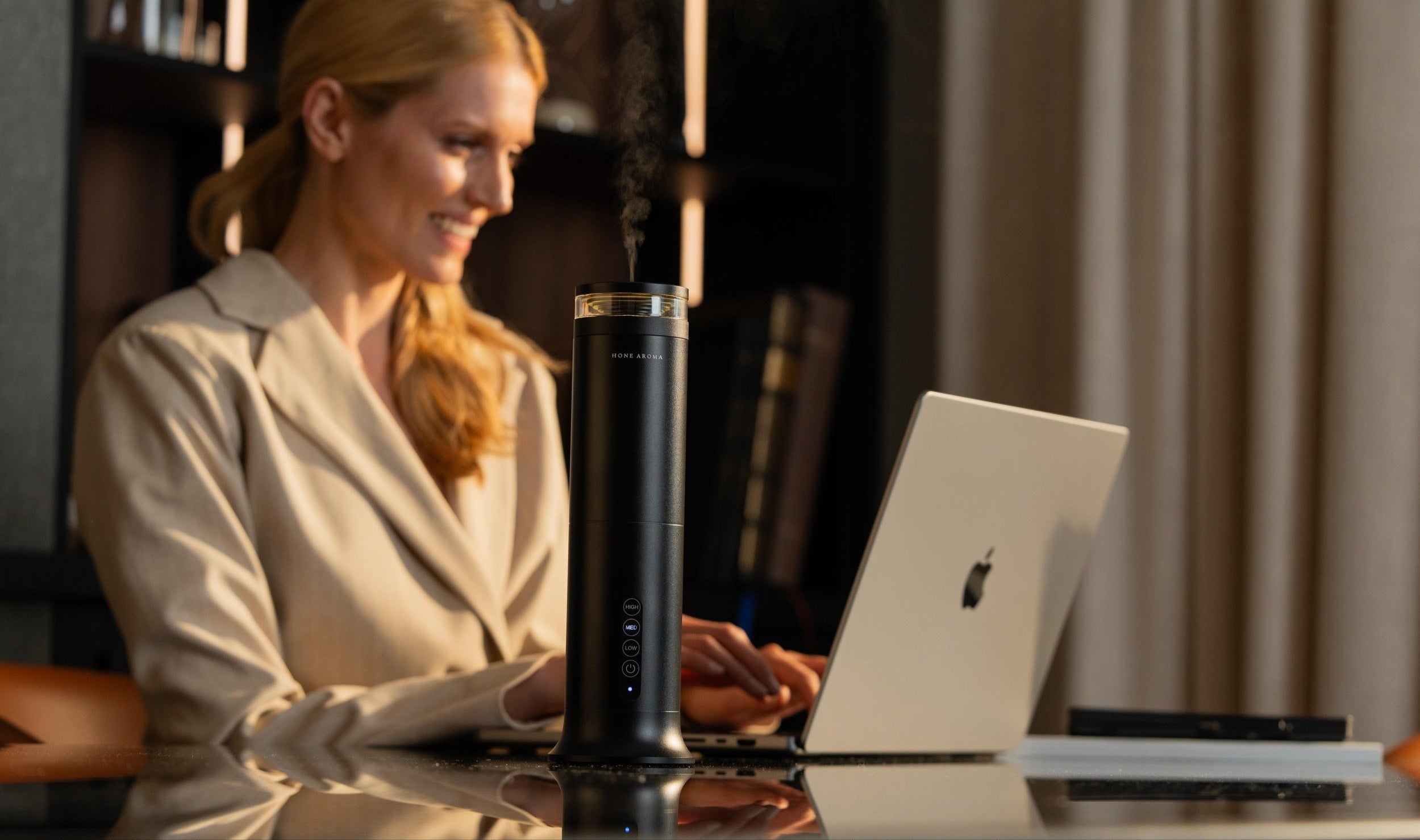 Woman using a laptop with a black pillar scent diffuser on a reflective surface